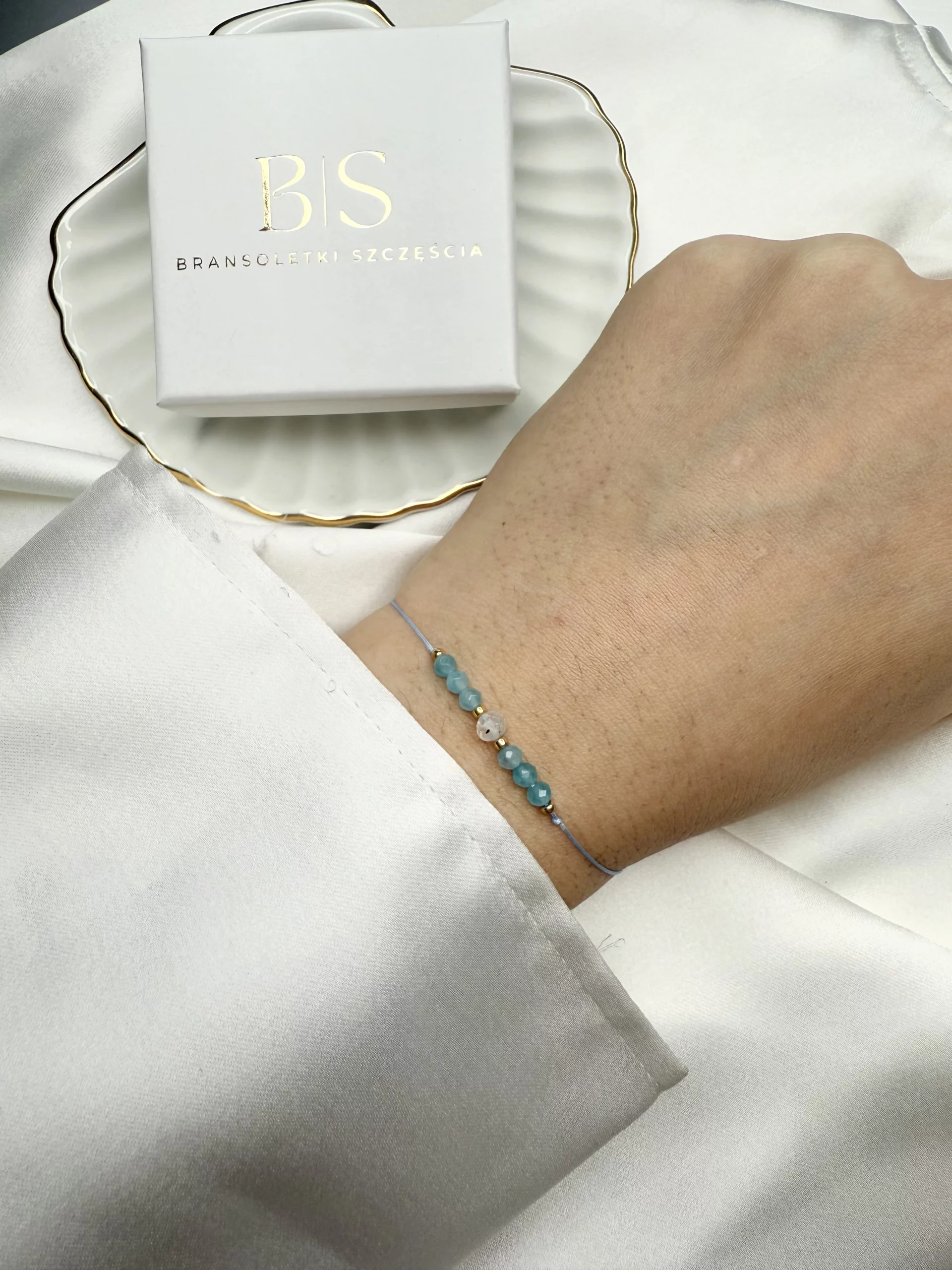 bransoletka z kamieniem księżycowym na nadgarstku, turkusowa nić, złote koraliki