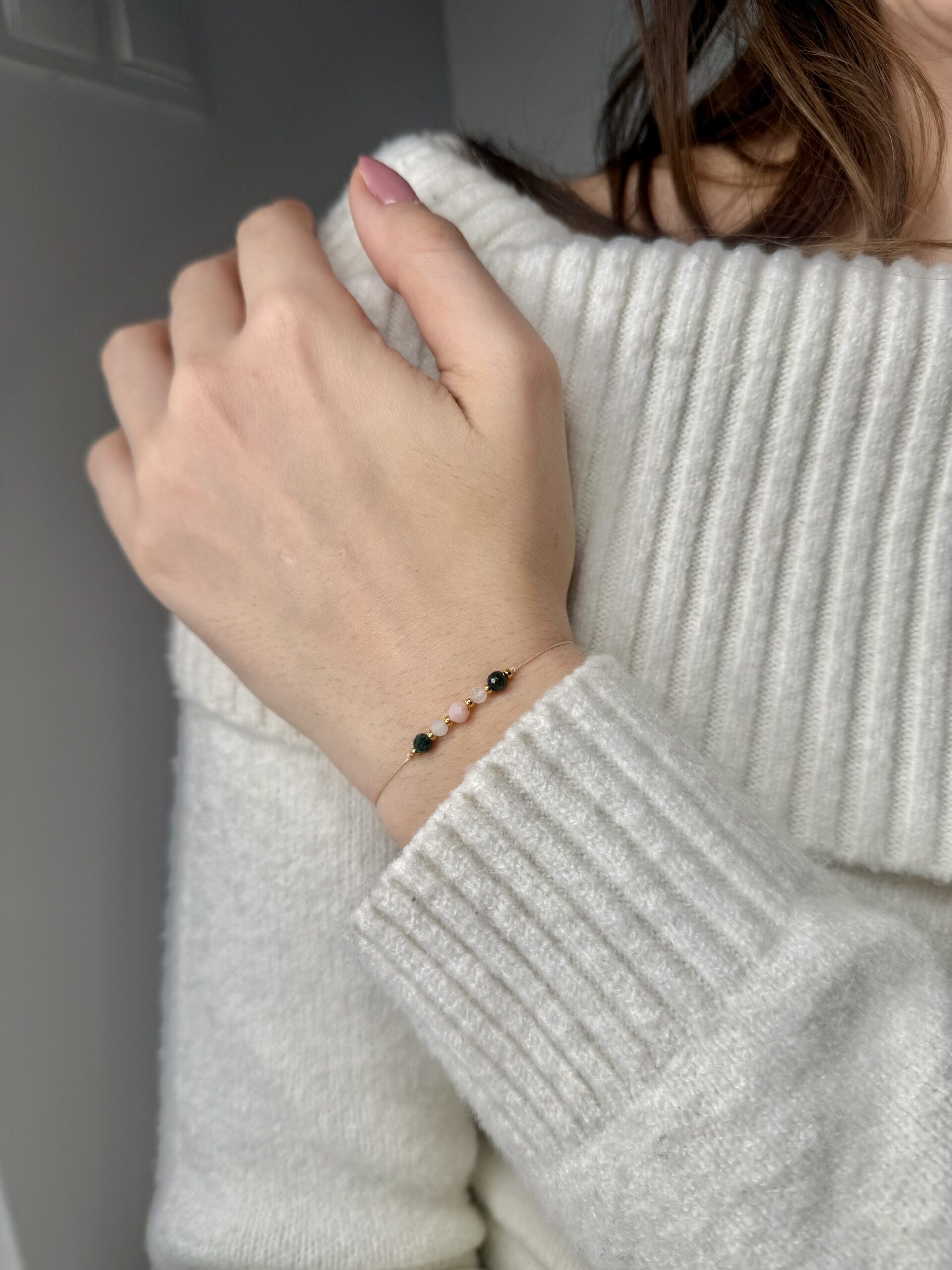 ręcznie robiona bransoletka zodiakalnego raka z naturalnymi kamieniami opal, akwamaryn i szmaragd, na nadgarstku.