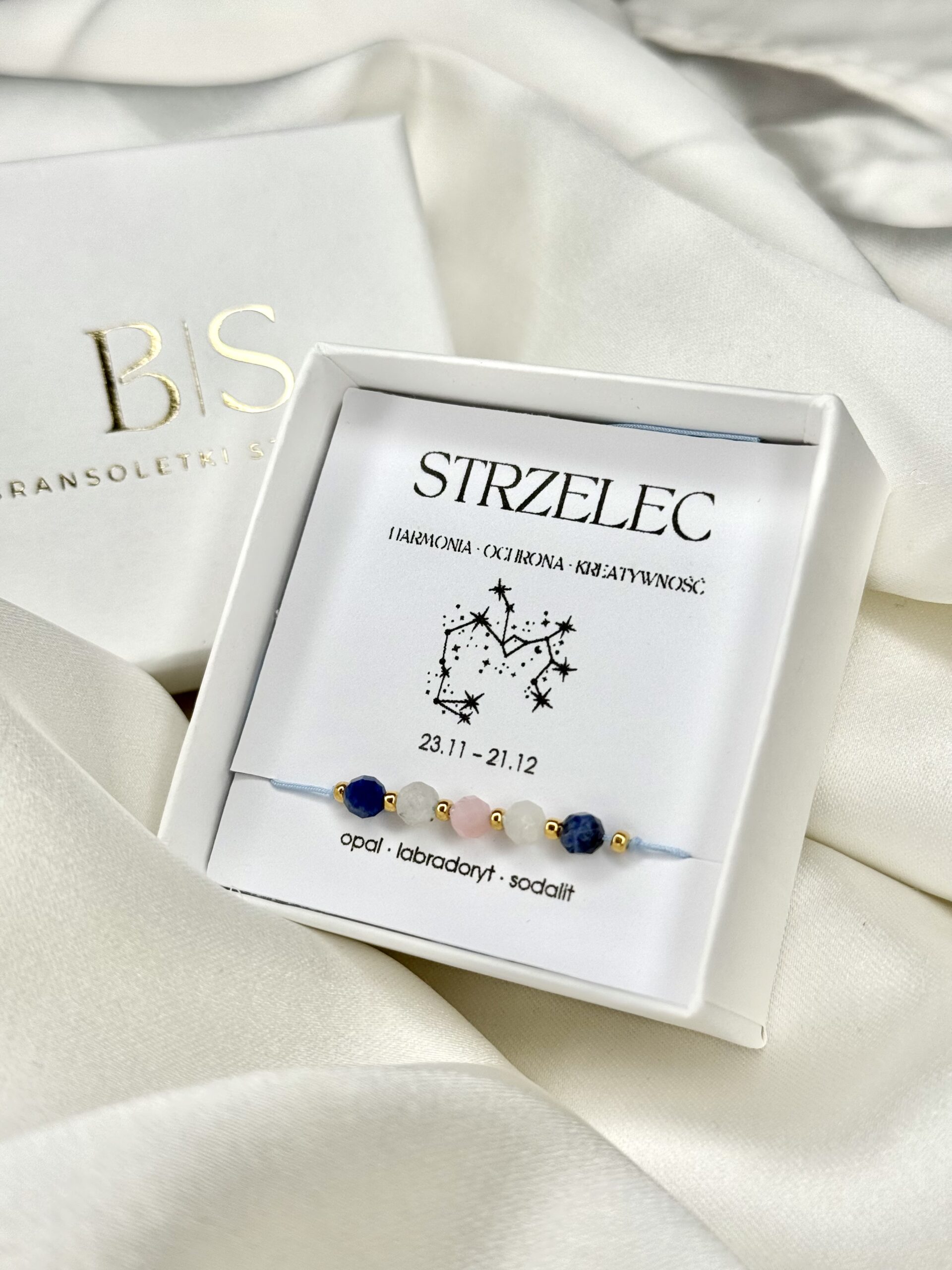 Bransoletka zodiakalna Strzelec w białym pudełku prezentowym na białym tle.