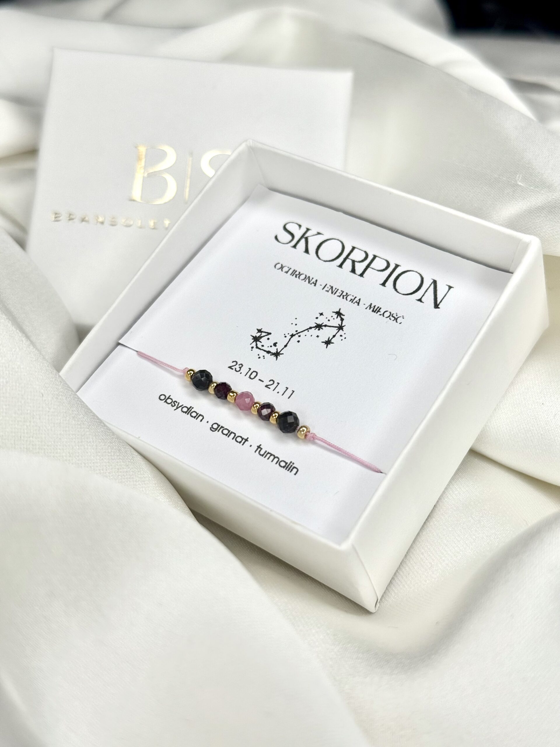 Bransoletka zodiakalnego Skorpiona w białym pudełku na białym tle.