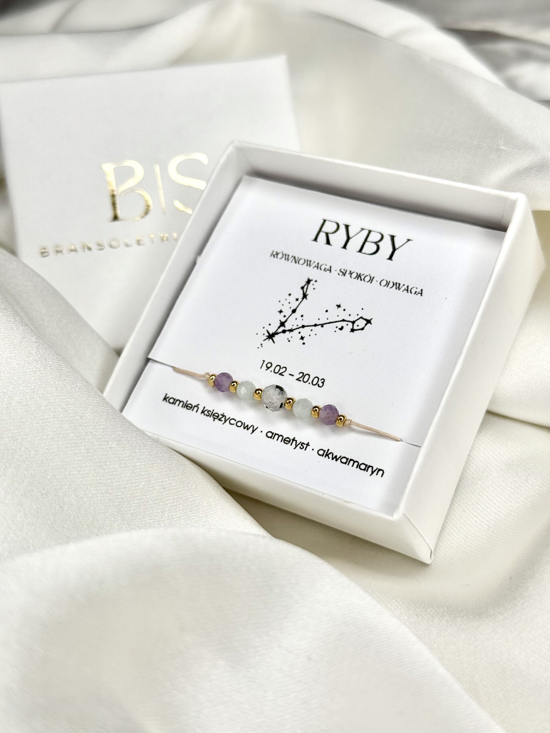 Bransoletka zodiakalna Ryby w białym pudełku na białym tle.