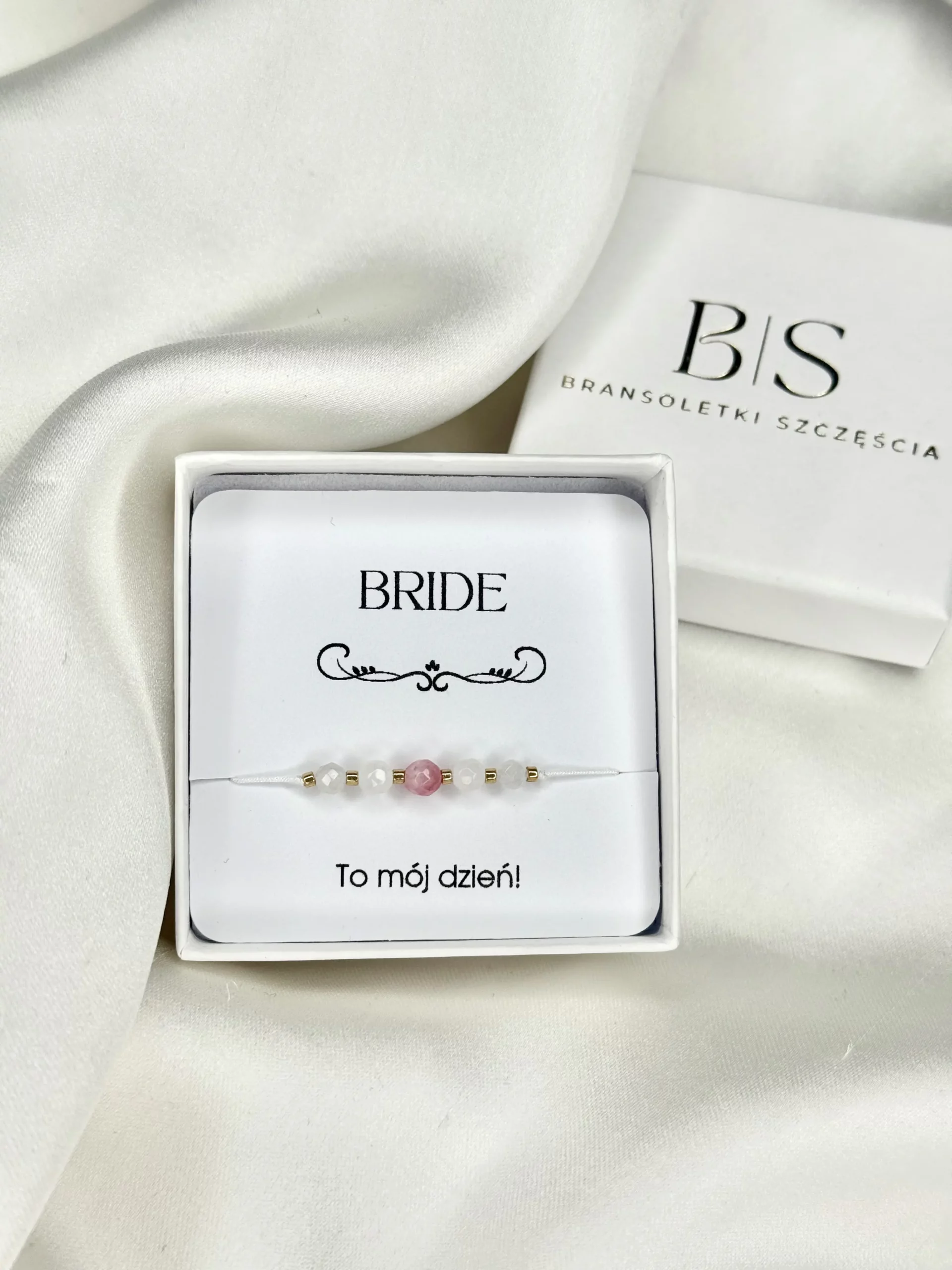 Bransoletka BRIDE 1 na białym sznurku, z kamieniami naturalnymi i złotymi koralikami, zaprezentowana w pudełku na ozdobnej karcie.