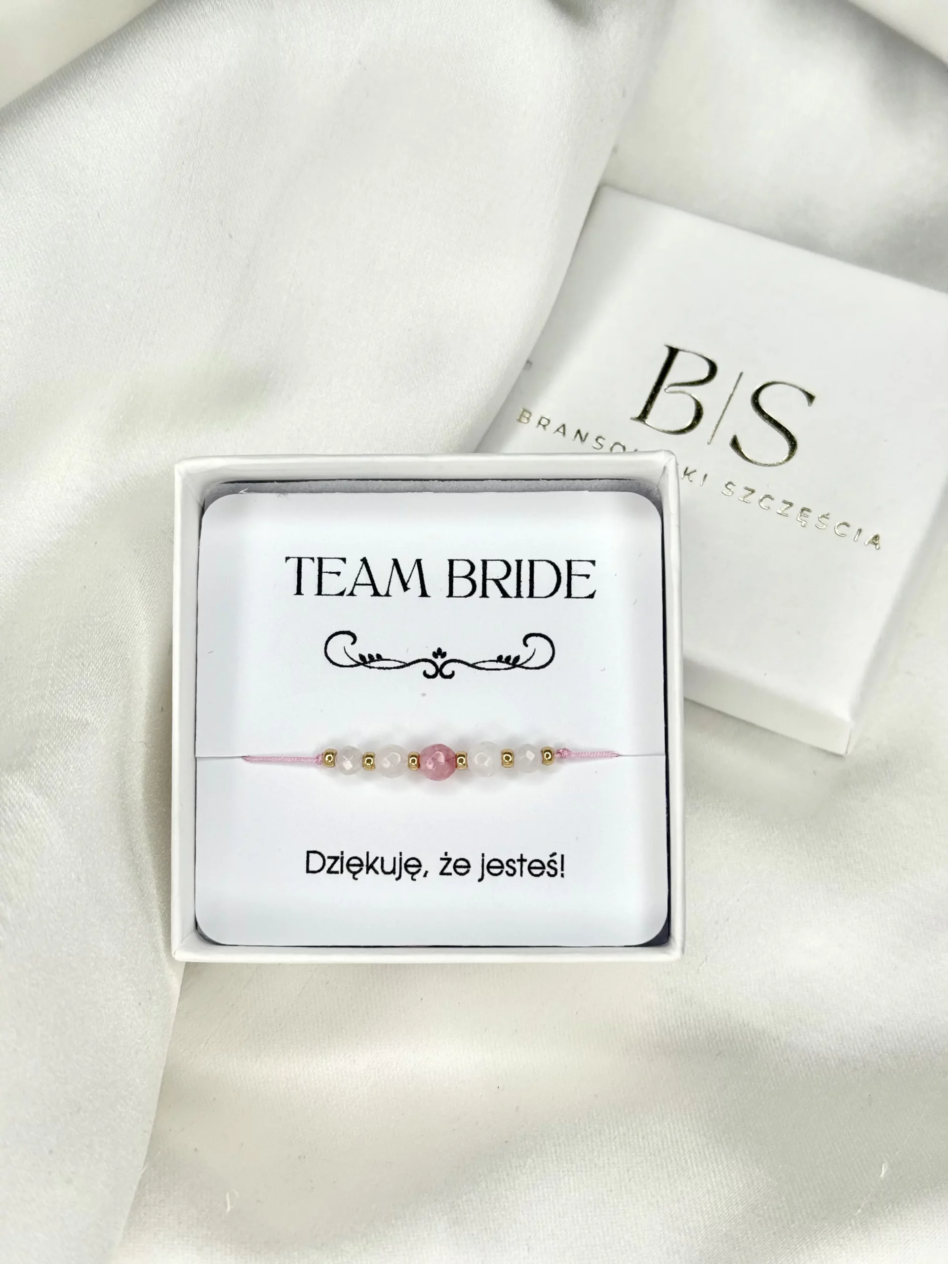Bransoletka TEAM BRIDE z kamieniami naturalnymi i złotymi koralikami na różowym sznurku, ułożona w eleganckim pudełku.