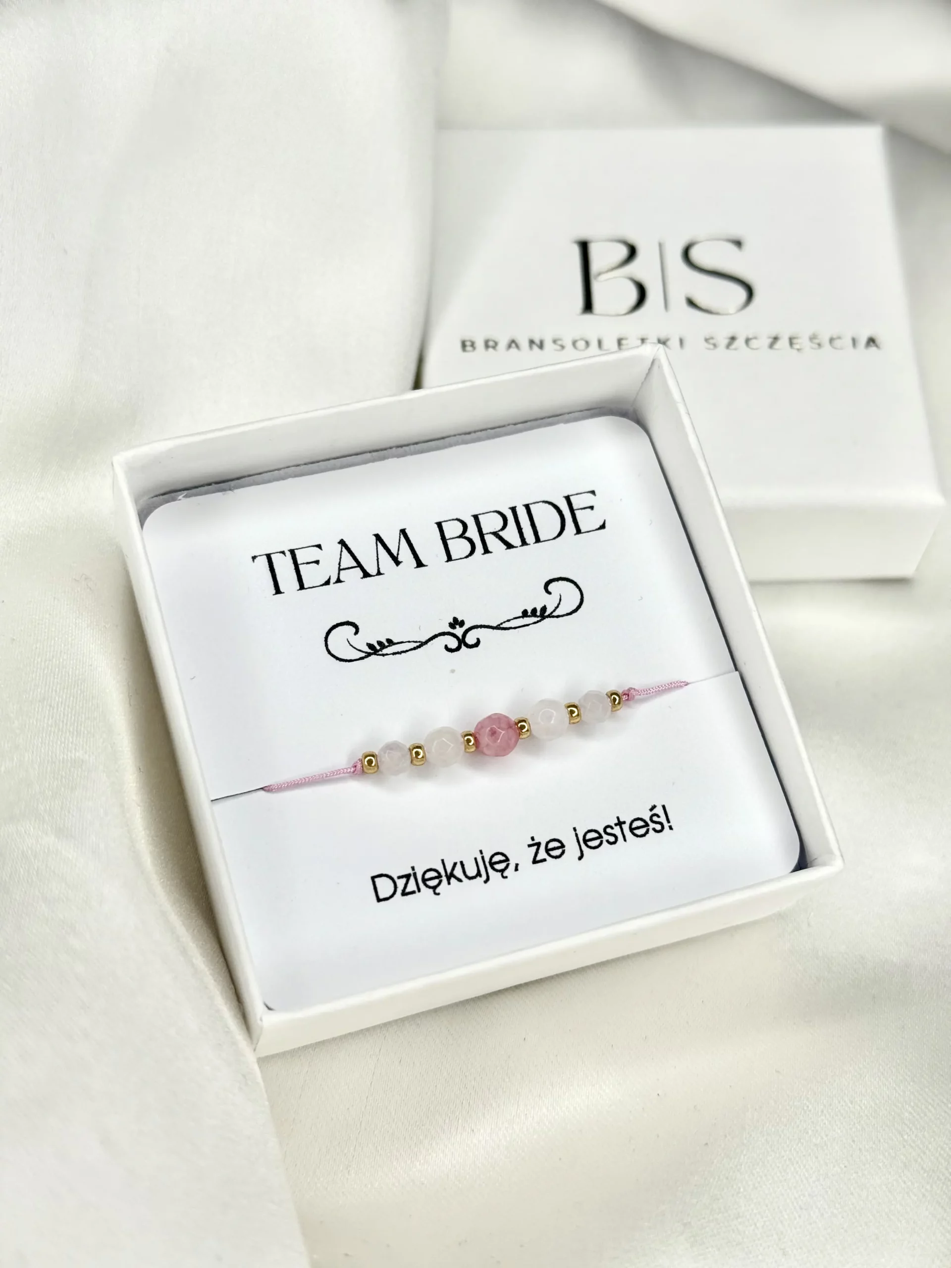 Bransoletka TEAM BRIDE na różowym sznurku z naturalnymi kamieniami i złotymi dodatkami, prezentowana w pudełku na ozdobnej karcie.